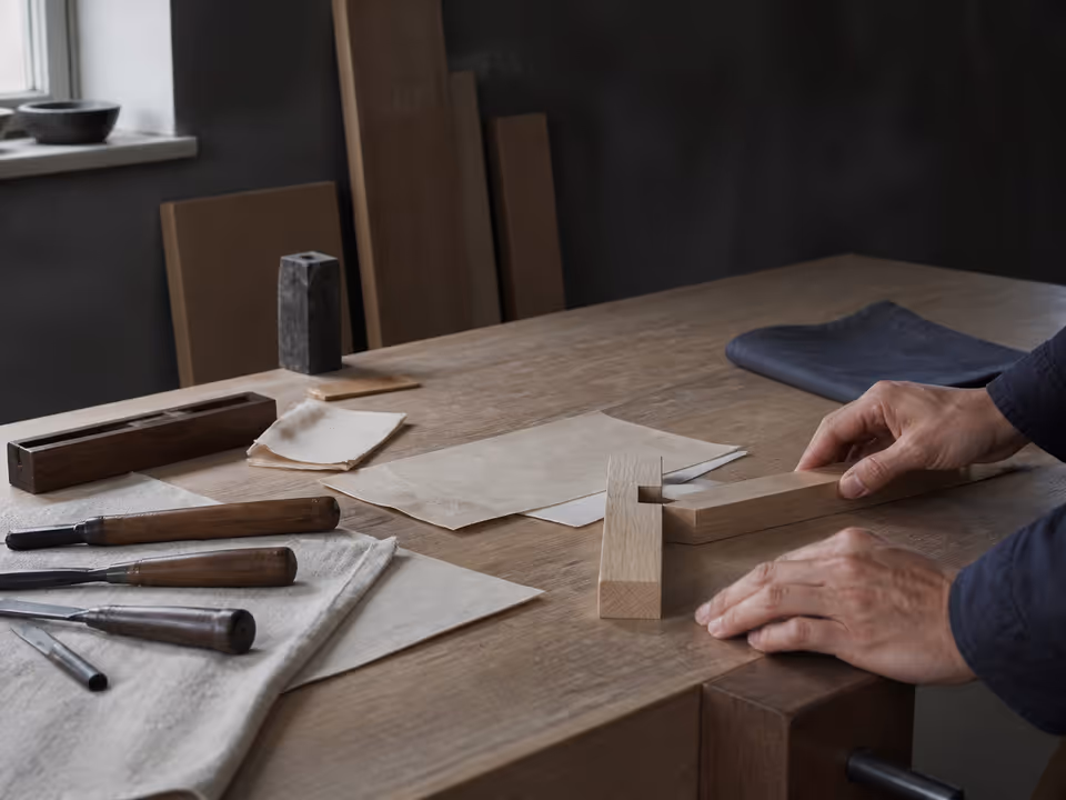 Craftsperson arranging tools and an unfinished wooden joint on a workbench