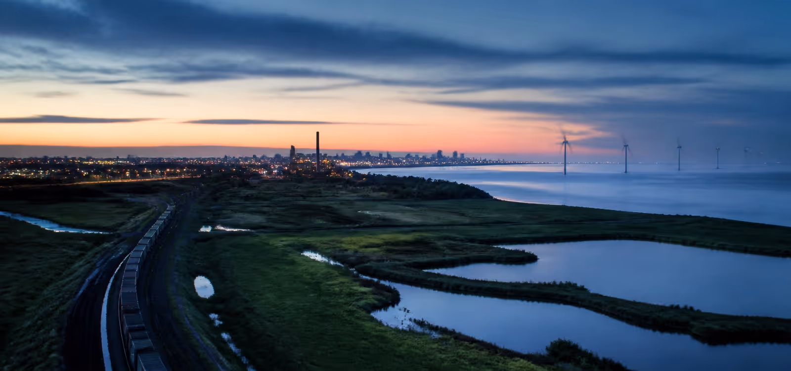 Coastal infrastructure, rail, energy, and wetlands meeting at dawn